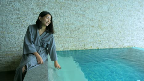 el enfoque suave y borroso de las mujeres asiáticas sentadas en la piscina privada del complejo y usan su mano para salpicar el agua en vacaciones