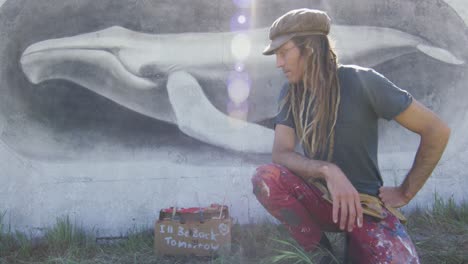 video portrait of smiling caucasian male artist with dreadlocks in front of whale mural on wall