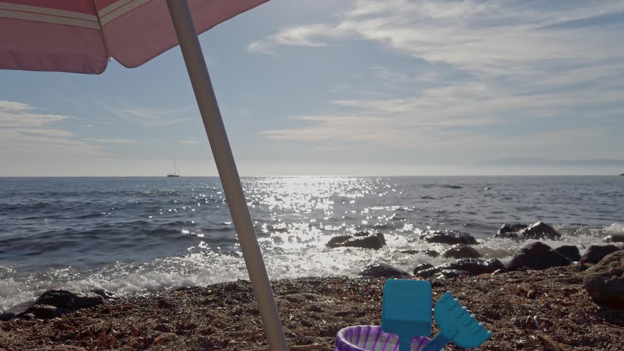 conjunto de cubo de juguete con rastrillo y pala debajo de la sombrilla en la playa