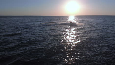 a woman on a jet ski performs a tight turn on an empty ocean during sunset, static drone view