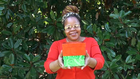 Slow-zoom-in-Medium-shot-of-Happy-smiling-black-woman-wearing-glasses-looking-directly-at-camera-holding-two-small-Christmas-gift-boxes