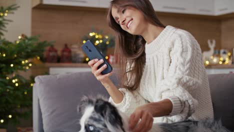 Frau-Chillt-Mit-Hund-Auf-Sofa-Und-Handy-Während-Der-Weihnachtszeit.