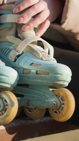 un primer plano de una persona caminando a un banco del parque y sentada, colocando sus patines a su lado. el banco está en foco, con la persona sin rostro