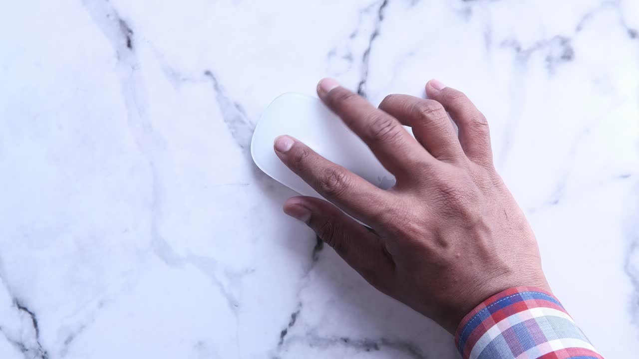 mano sosteniendo un ratón de computadora blanco en una superficie de mármol