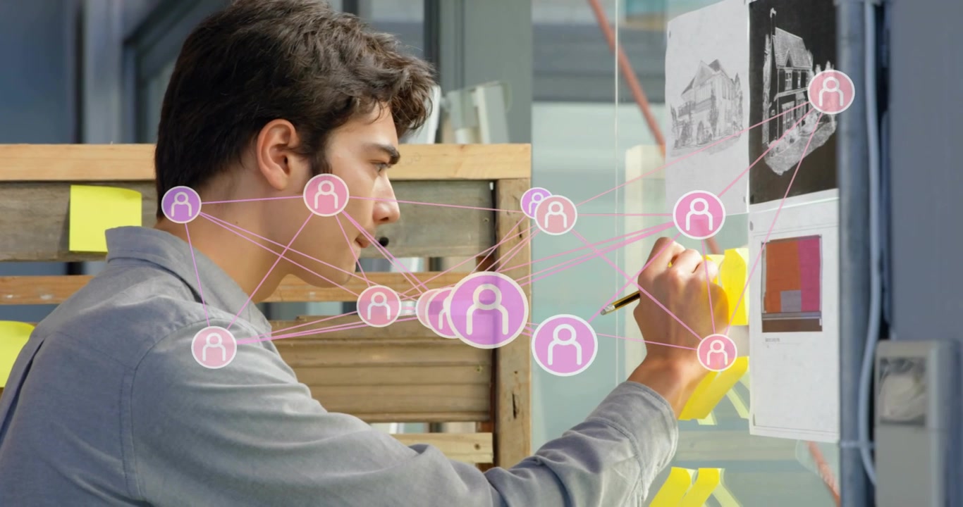 Diseñador buscando un lápiz, seleccionando una nota, escribiendo en una pizarra de cristal con iconos de realidad aumentada que muestran trabajo en equipo
