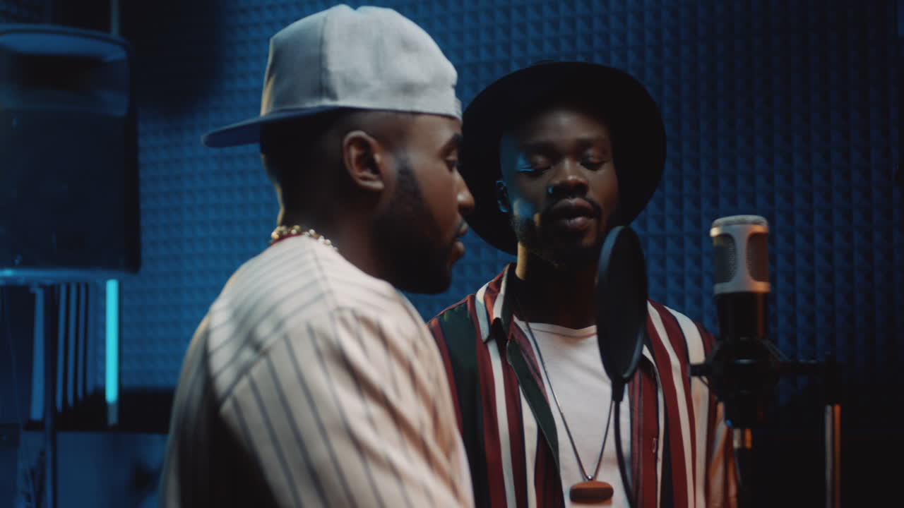 사운드 스튜디오의 마이크에 서서 함께 노래하는 두 명의 젊고 잘생긴 세련된 남자들과 가까이