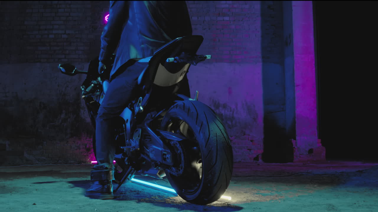 가죽 재을 입은 남성 바이커가 벽돌 벽에 네온 분홍색 표지판에 맞서 스포츠 바이크에 앉아 있습니다.