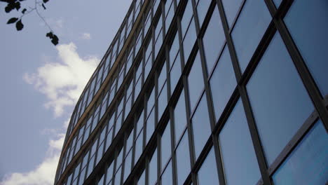 Frente-De-Vidrio-Del-Edificio-De-Oficinas-Contra-El-Cielo-Azul-Con-Nubes-Que-Pasan