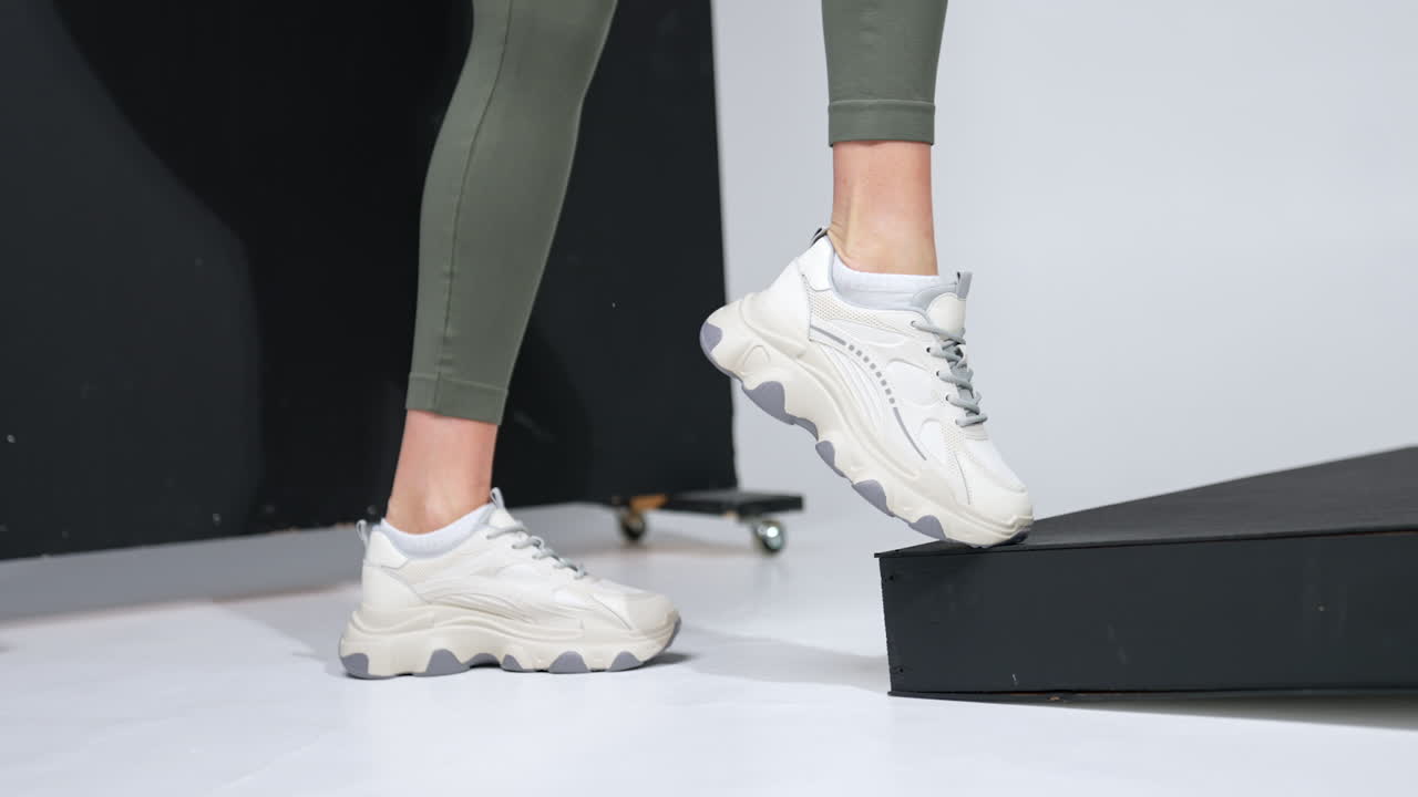 Model is fitting her trendy nice white sneakers. Fashionable comfortable footwear demonstrated in the studio.