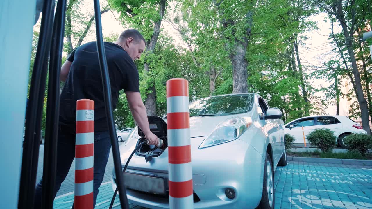 전기 자동차의 연료 충전 과정: 전기 에코 자동차가 충전하는 치 아래의. 전기 자동차 충전 치는 자동으로 열립니다. 남성 손이 발기 된 자동차를 입합니다.