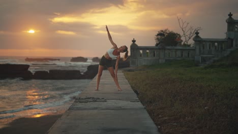 Fit-female-performing-Triangle-Pose-outside-at-seaside-with-dramatic-sunset