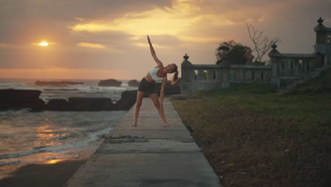 fit female performing triangle pose outside at seaside with dramatic sunset