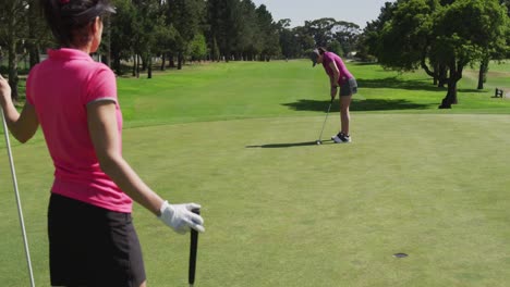 Two-caucasian-women-playing-golf-one-taking-shot-from-bunker