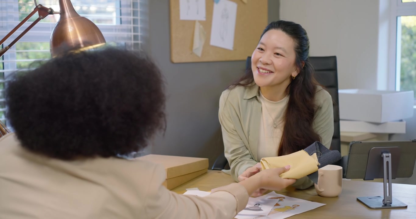 スタジオでスケッチを広げ、スウォッチを交換しながらサンプル用の生地を選ぶ多様な女性チーム