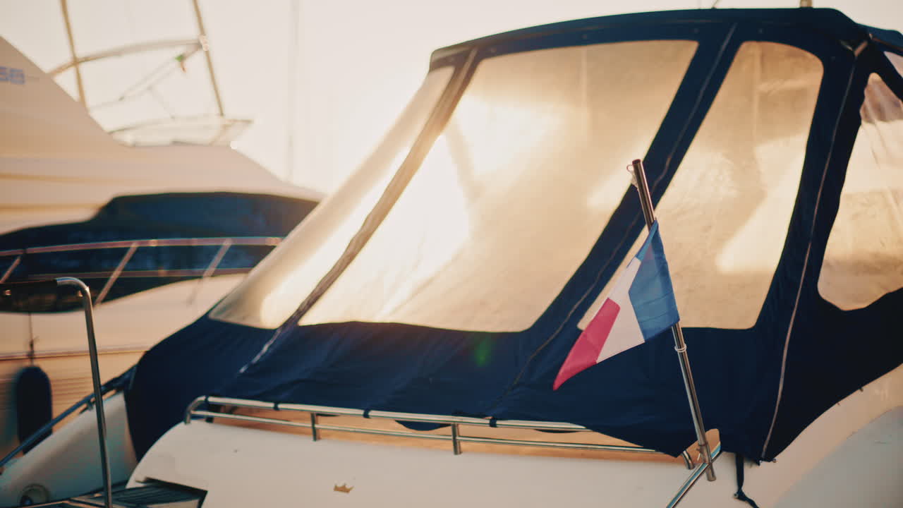 A French flag waves gently beside a sunlit boat canopy in a marina during early morning light