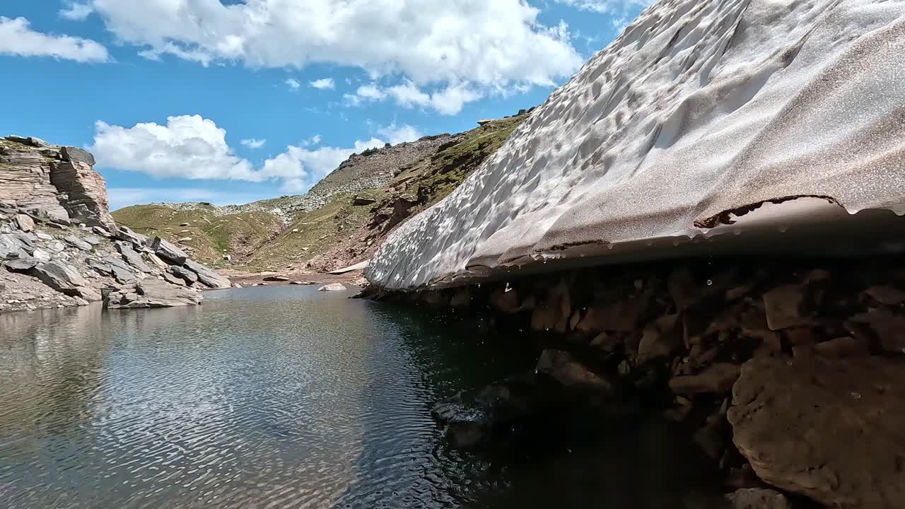Melting glacier edge touches a cold alpine pond surrounded by rocky slopes in Alpe Veglia Natural Park, Italian Alps
