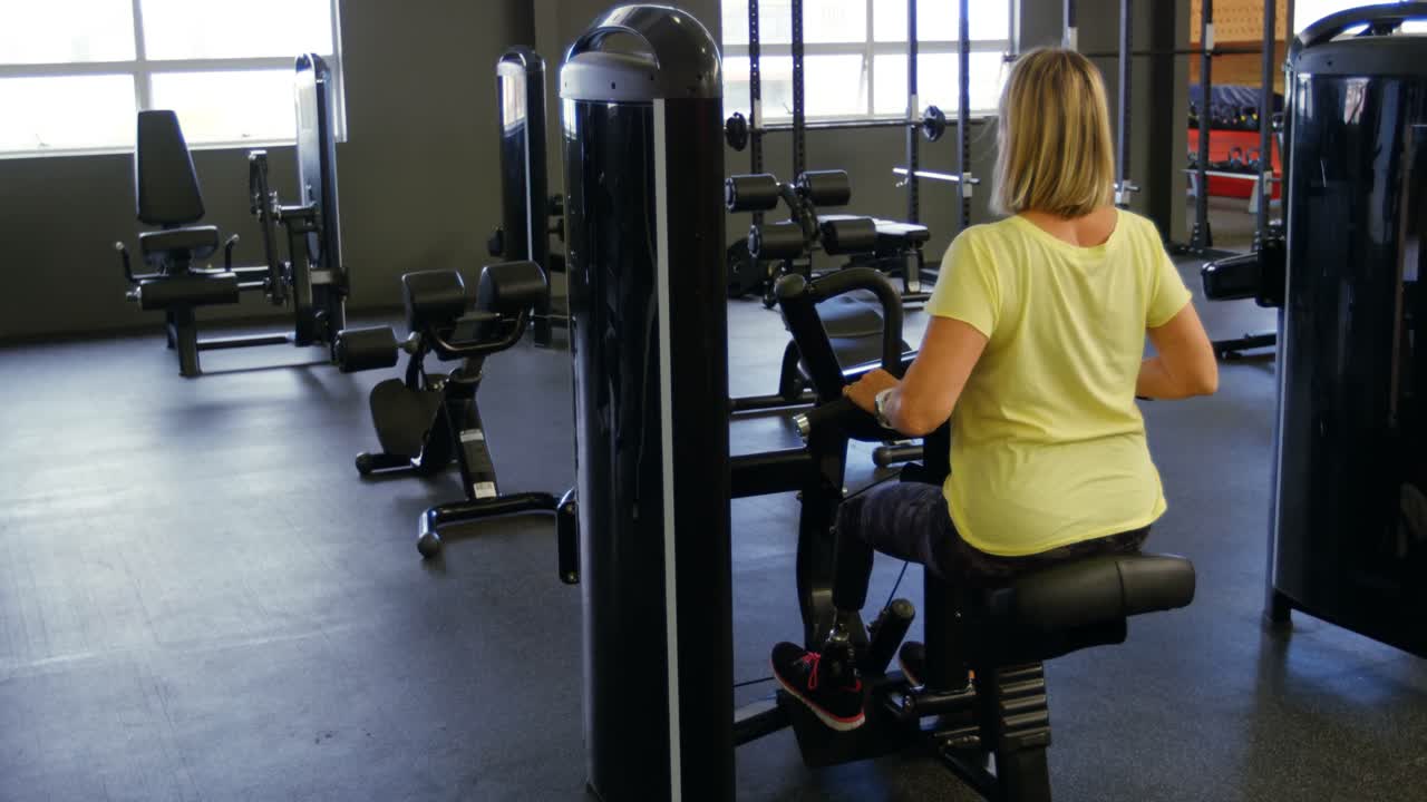 Senior woman doing back exercise on machine in fitness studio 4k