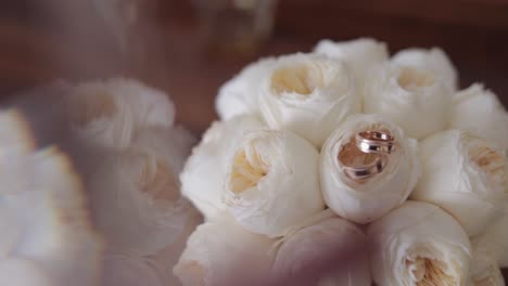 Wedding-golden-rings-lie-on-beautiful-wedding-white-rose-flowers-bouquet-on-the-brown-tablet