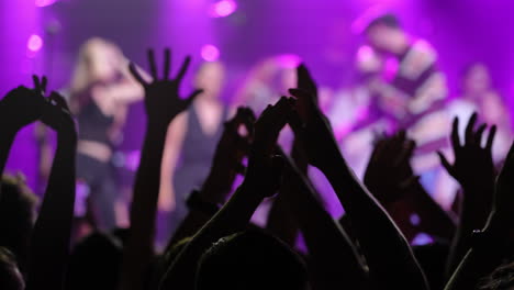 crowd of enthusiastic concertgoers with raised hands enjoying vibrant music and colorful lights
