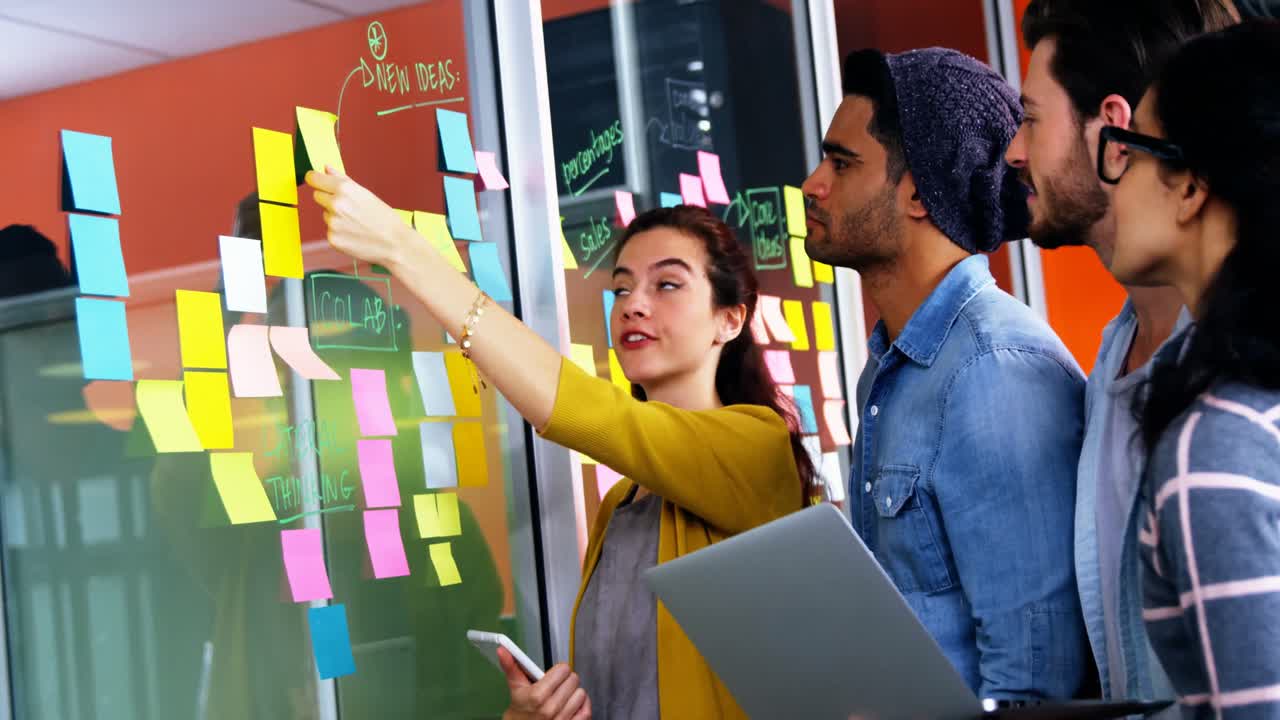 Smiling executives discussing over sticky notes on glass wall