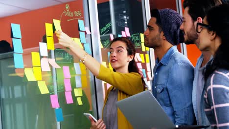 Smiling-executives-discussing-over-sticky-notes-on-glass-wall