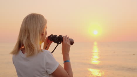 Young-Romantic-Woman-Looks-At-The-Sunrise-Over-The-Sea-Of-Pink-Color-Uses-Binoculars-4k-Video