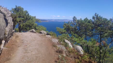 sendero forestal salvaje junto al acantilado con el mar y la costa al fondo en un día claro y soleado, tiro que avanza, movimiento a pie, islas cíes, pontevedra, galicia, españa-1