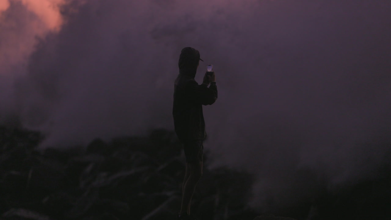 Teenager films large wave breaking on jetty at sunset