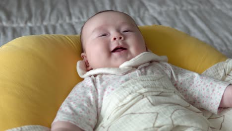 infant baby smiling while lying on a soft yellow cushion