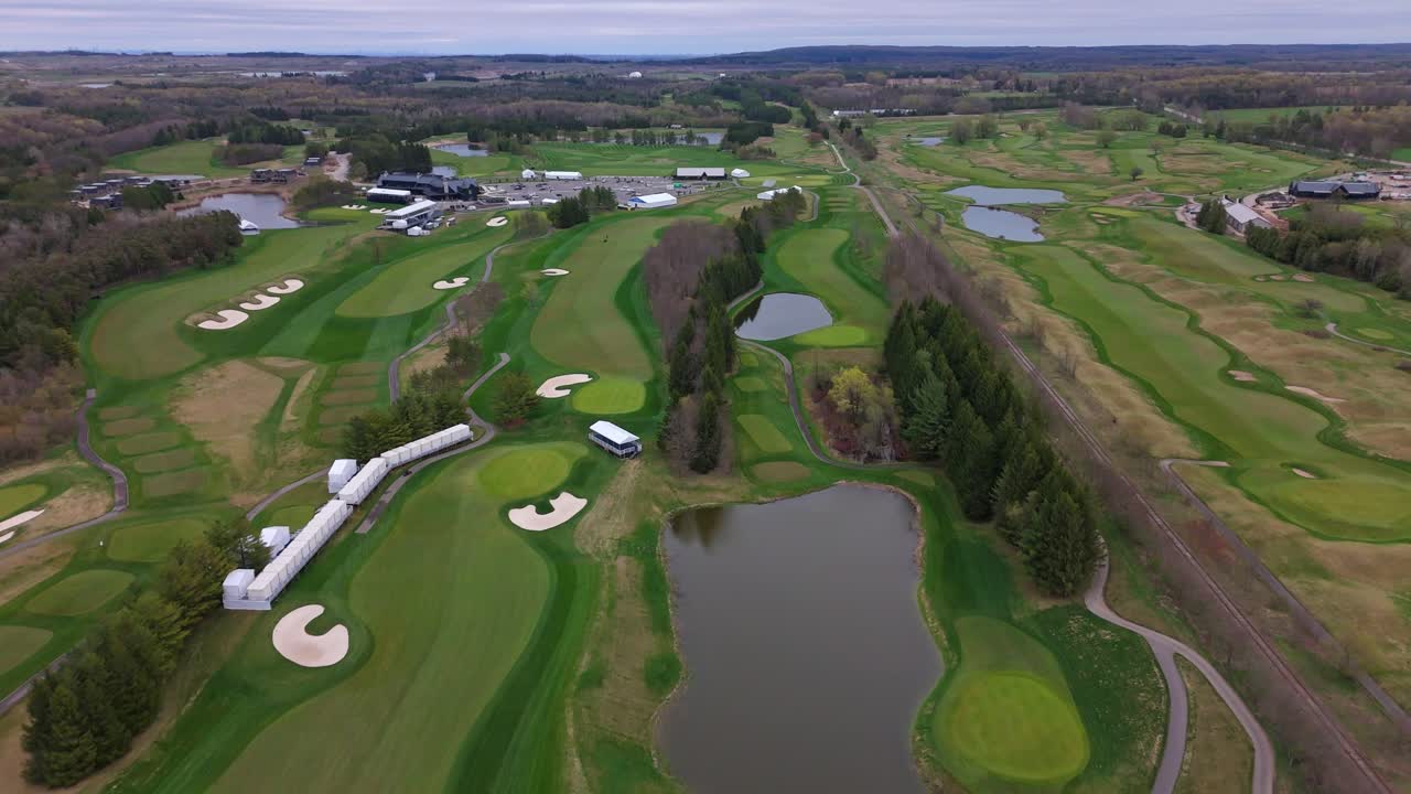 Lake with green golf course in Canada during cloudy day. Aerial top down flyover.Green grass fields in forest landscape. Wide shot.
