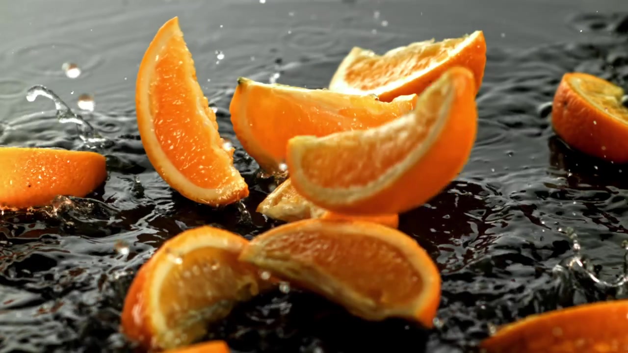 Appelsinskiver faller og plasker i mørkt vann i sakte film