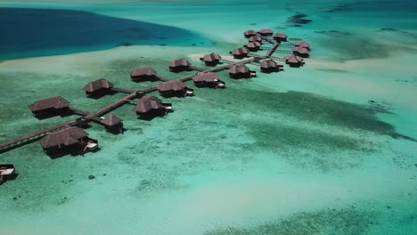 aerial, descending, drone shot, towards a pier full of bungalows on water, surrounded by the shallow, turquoise ocean, on a sunny day, on the conrad rangali island, in maldives