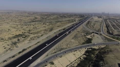 Una-Vista-Aérea-En-Cámara-Lenta-De-Una-Carretera-Y-Una-Ciudad,-Los-Arrastreros-Pesados-Y-Los-Coches-Se-Mueven-Por-La-Carretera,-Se-Conecta-Un-Intercambio