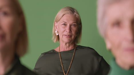 Blonde-Mature-Woman-Wearing-Green-Shirt-Looking-At-Side-Posing-On-Green-Background-With-Two-Blurred-Women-In-Foreground,-Then-Looking-At-Camera