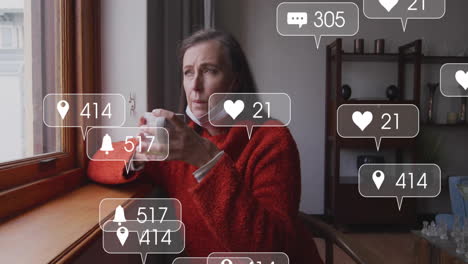 mature woman sitting by window, holding coffee mug, viewing floating social media notifications
