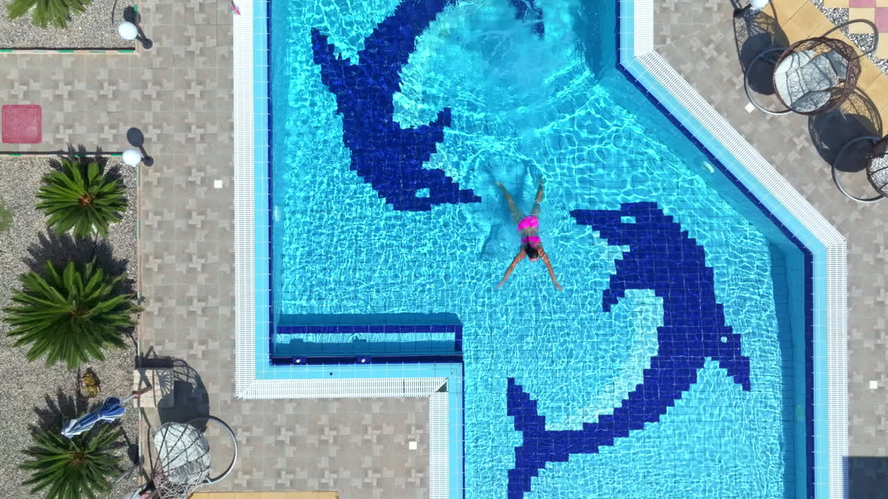 Dronebillede i fugleperspektiv af en kvinde, der hopper i en pool for at svømme i en villa på en solskinsdag