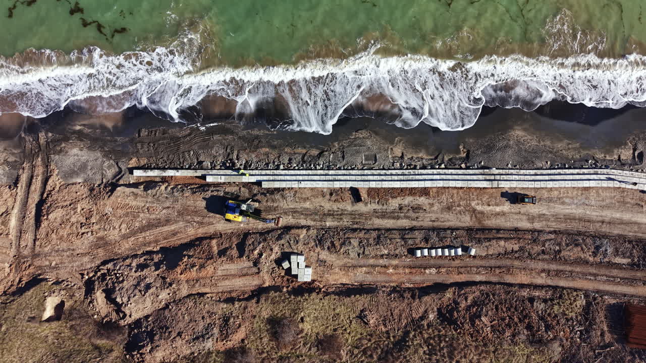 Lavori di costruzione lungo la costa vicino alla spiaggia con macchinari pesanti e onde che si infrangono sullo sfondo