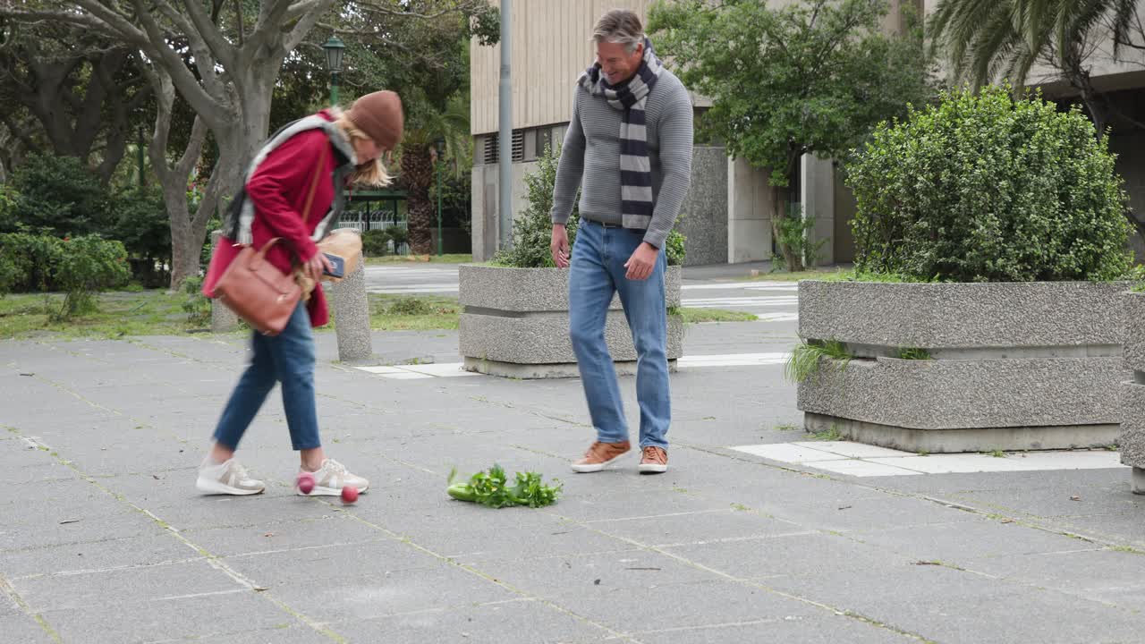 Et ældre par går på en plads med en indkøbspose, der flosser, og indholdet spildes, mens de bøjer sig ned for at samle det op.