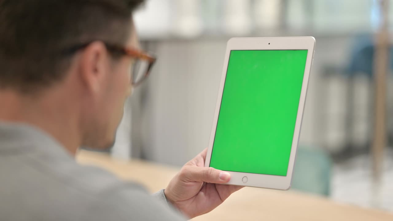vista trasera de un hombre de mediana edad mirando una tableta con pantalla cromada