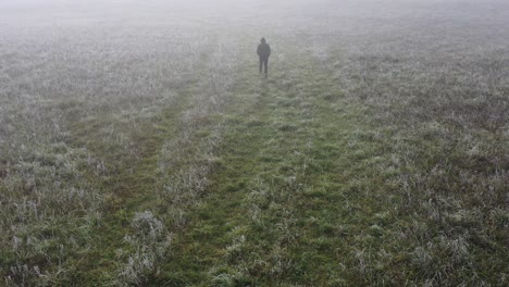 Luftaufnahme-Eines-Einzelnen-Mannes,-Der-Am-Herbstmorgen-Im-Nebel-Auf-Der-Wiese-Spaziert-Und-Drohnenaufnahmen-Verfolgt