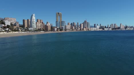 Aerial-flight-towards-Benidorm-City-with-modern-architectures-and-sandy-beach-during-sunny-day,-Spain---Wide-shot