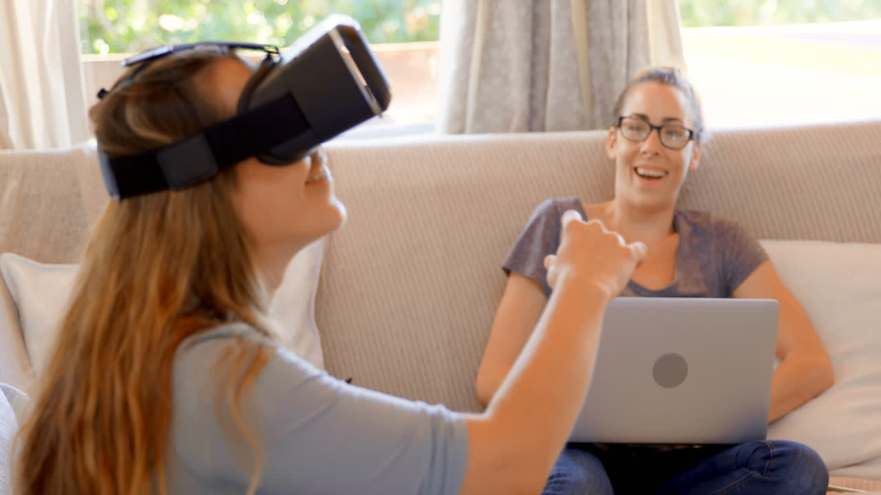 una pareja de lesbianas usando auriculares de realidad virtual y portátil en la sala de estar 4k