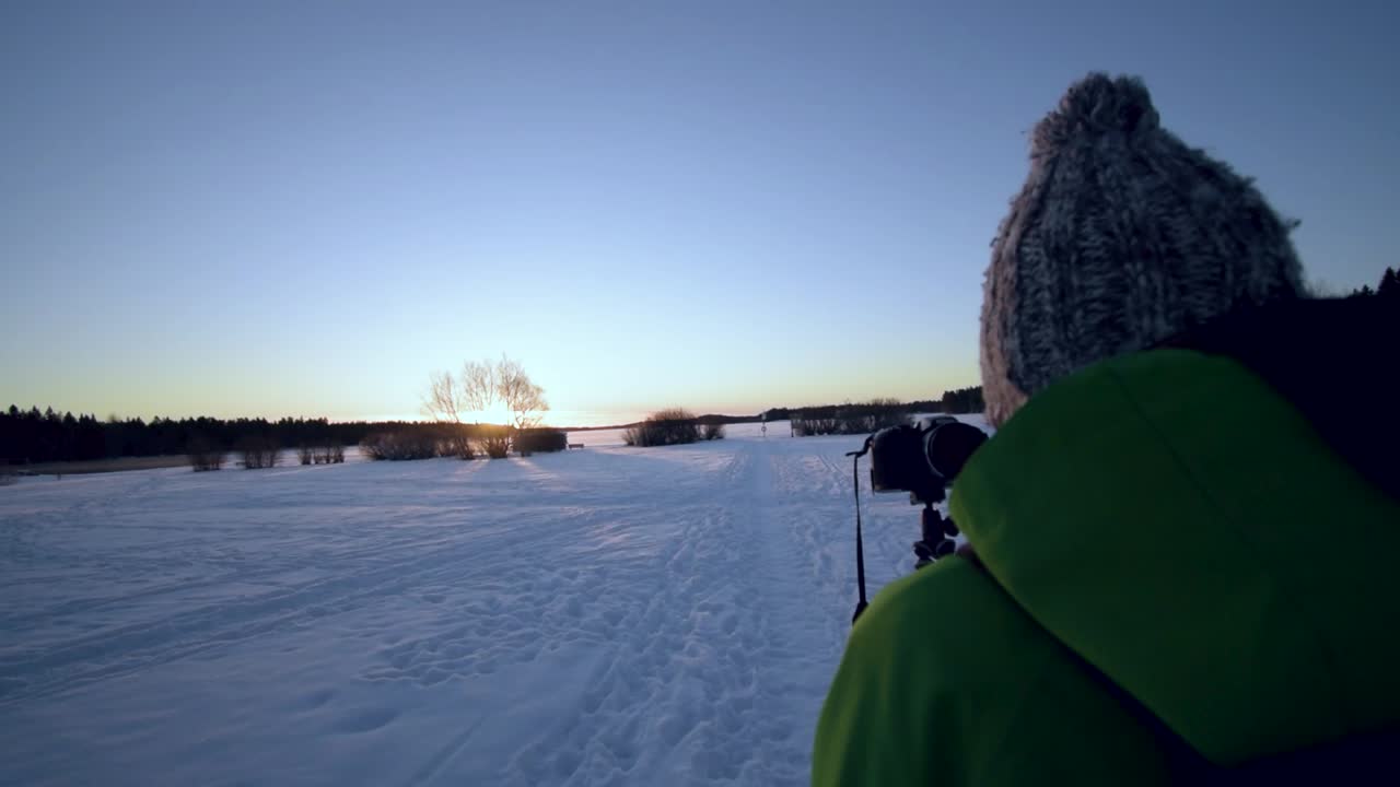 Vloggaaja kuvaa itseään kameraa pidellen auringonlaskun aikaan talvisessa ihmemaassa.