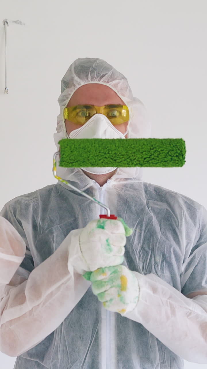 young people wearing transparent coveralls with hoods and masks ready to repair house holding rollers in green paint