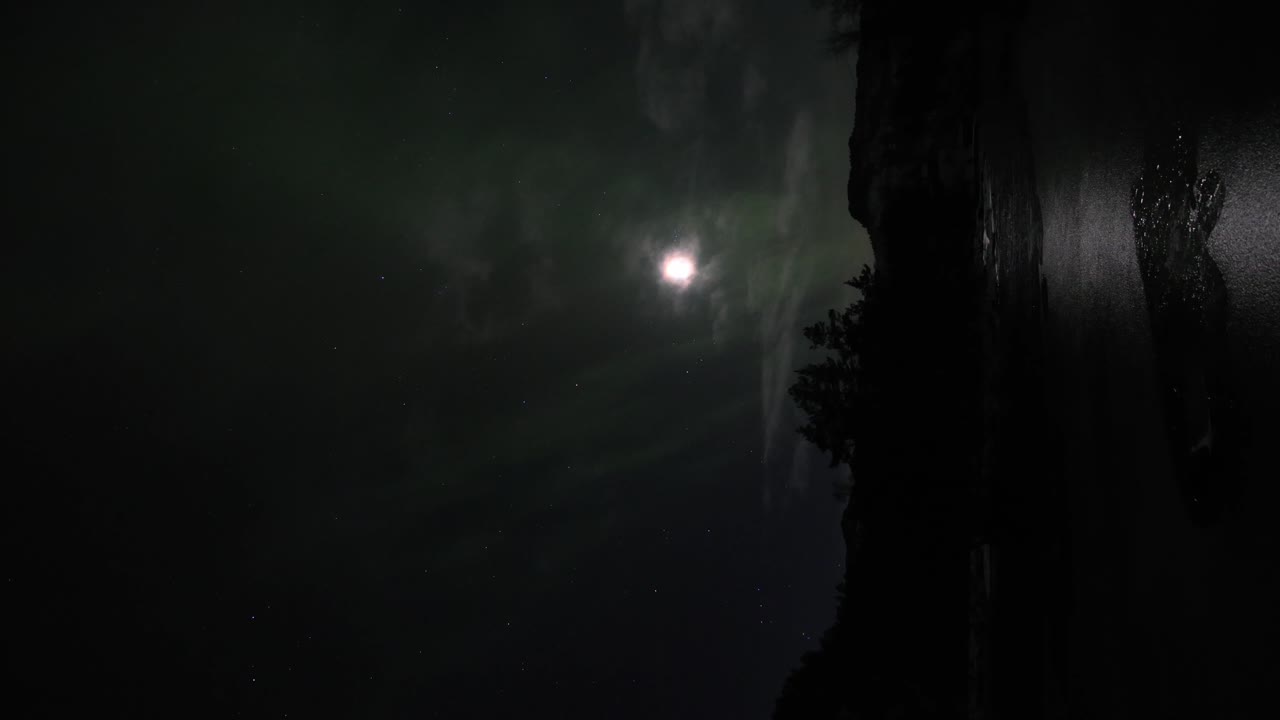 Aurora boreale di bassa intensità che danza lentamente davanti alla luna piena fuori Bergen, Norvegia - Verticale