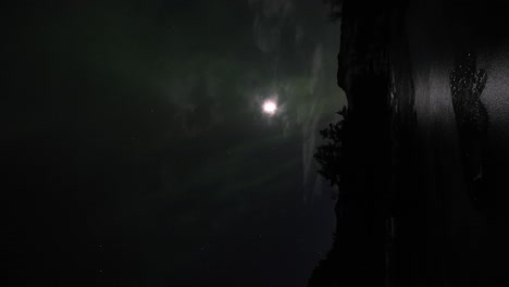 northern light aurora borealis with low strength slowly dancing in front of full moon outside bergen norway - vertical