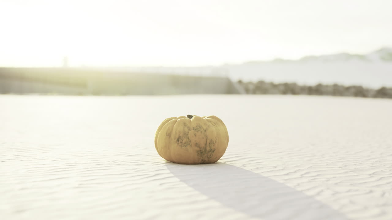 Golden pumpkin rests on smooth white sand under soft sunset light