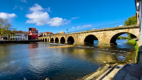 Low-angle-view-of-roman-bridge-of-Aquae-Flaviae,-Chaves-Vila-Real-Portugal-at-sunrise-as-water-flows-below