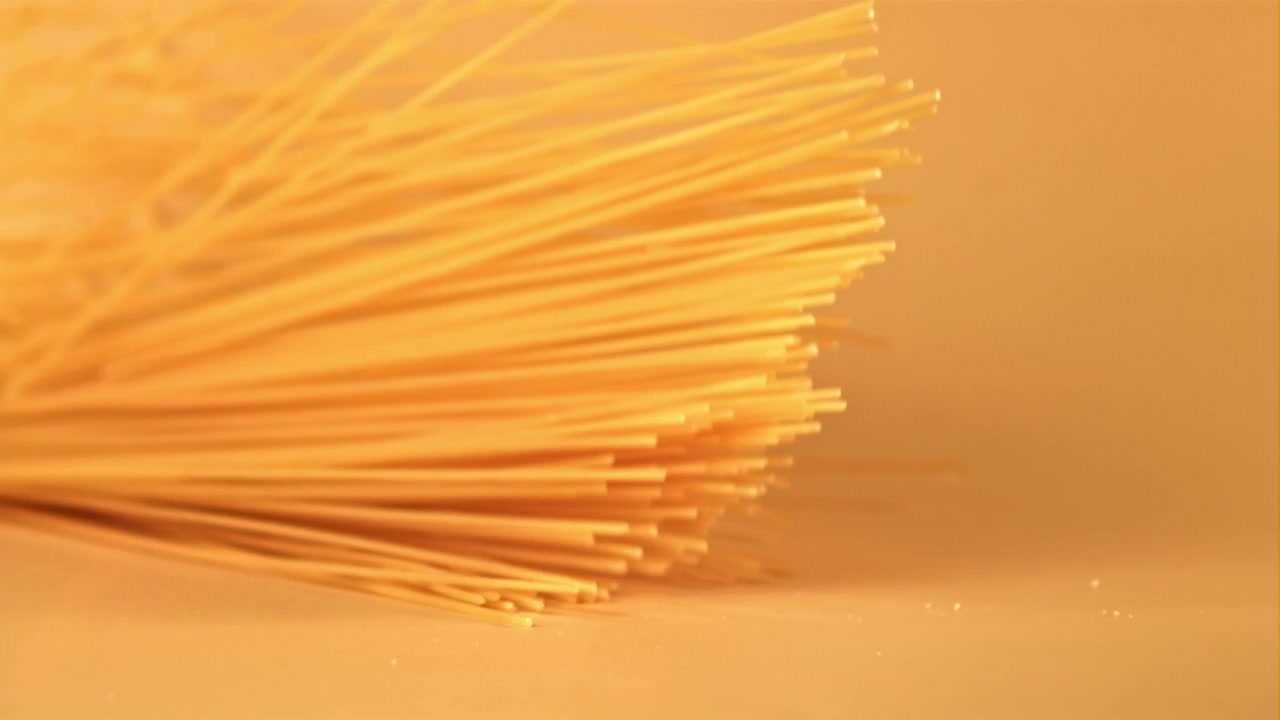 Spaghetti secchi che cadono su una superficie gialla calda