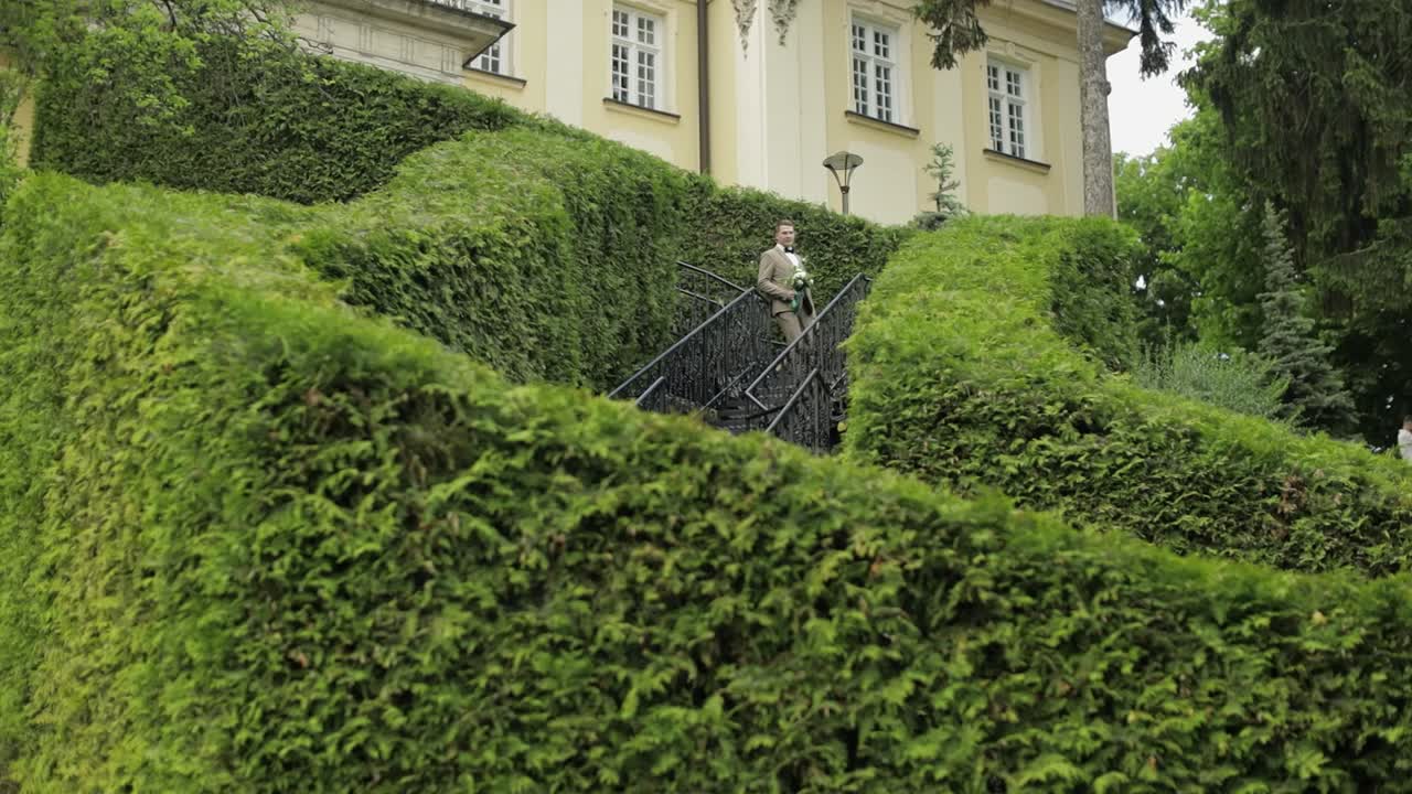 Lo sposo scende le scale tra gli alti cespugli con un bouquet da sposa per la sua amata.